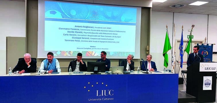 Sei relatori seduti a un tavolo con un drappo blu e il logo «LIUC Università Cattaneo»; alle loro spalle uno schermo con un elenco di nomi e immagini di palloni; a destra bandiere e un leggio.