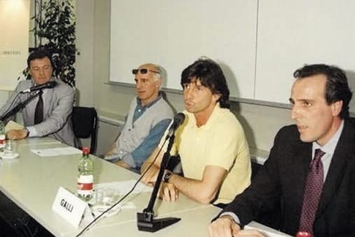 Quattro persone sedute a un tavolo di conferenza con microfoni; davanti a una di loro un cartellino con la scritta «Galli»; uno degli uomini indossa una maglia gialla.