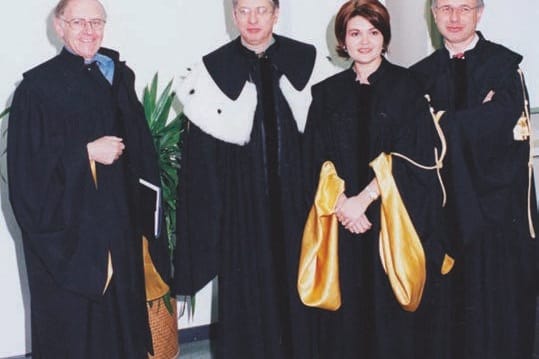 Quattro persone in toga nera con mantelline bianche e dorate posano in piedi una accanto all’altra: tre uomini e, al centro, una giovane donna dai capelli scuri.