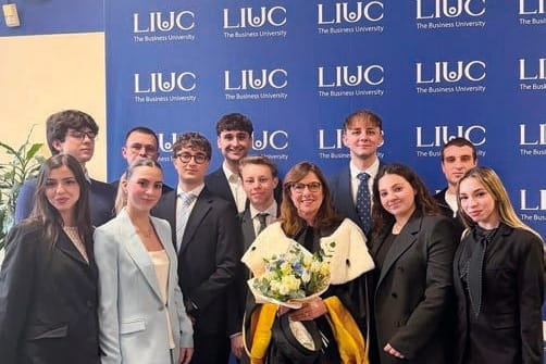 Un gruppo di studenti in abiti scuri posa davanti a un pannello blu con il logo LIUC; al centro una donna in toga con una mantellina gialla e bianca regge un mazzo di fiori.